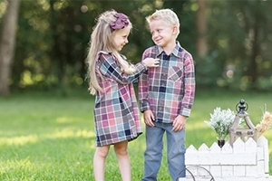 Boy and girl siblings wearing matching plaid outfits in the lawn
