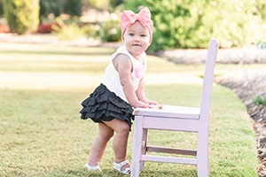 Baby girl in the garden wearing a pink bow and a ruffled skirt