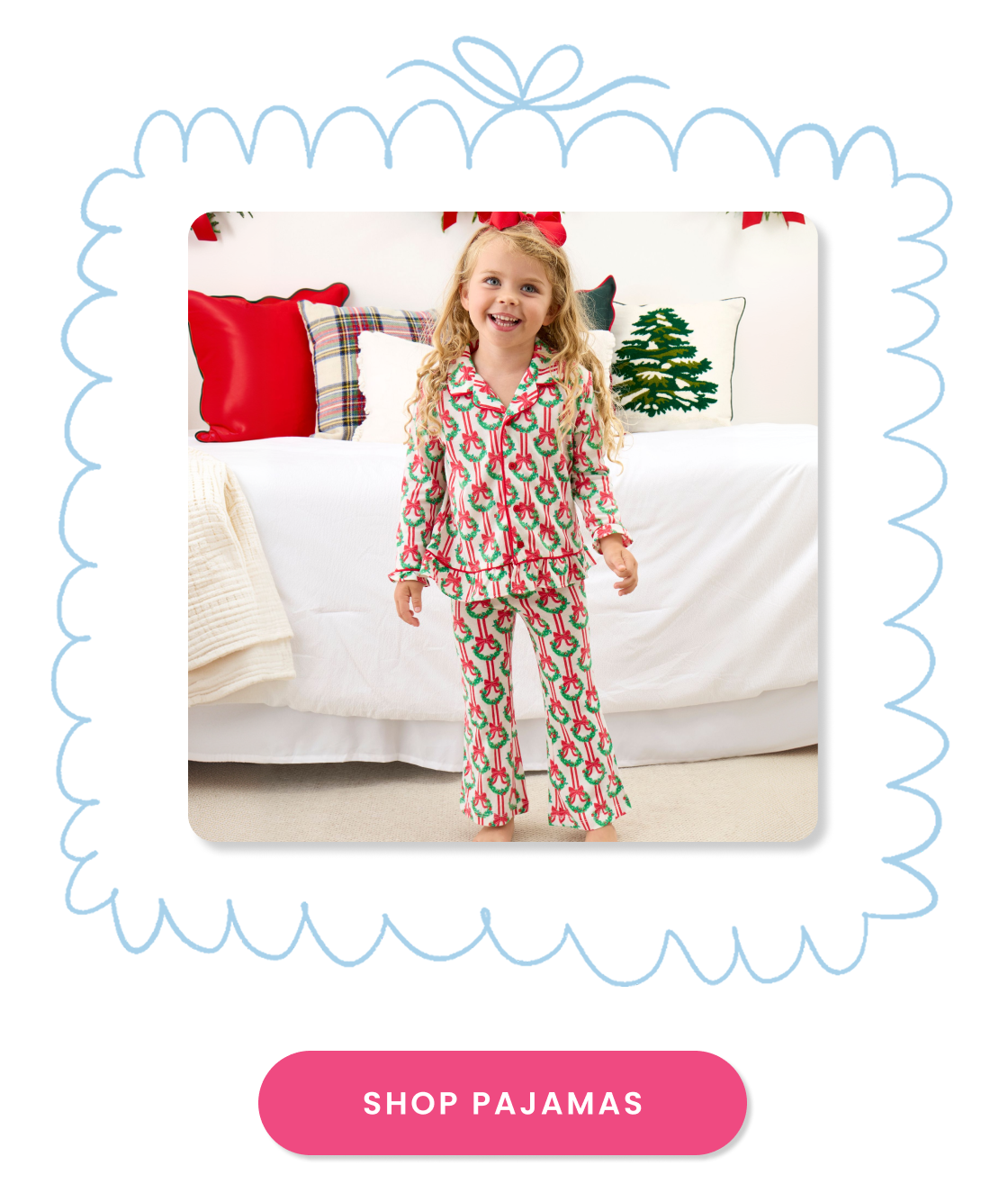 Promotional image showing a child wearing holiday pajamas with wreath and bow print, standing in a festive bedroom. Call-to-action button reads ‘Shop Pajamas.’