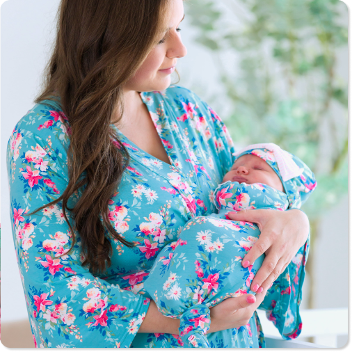 Promotional image showing an adult holding a newborn wrapped in a matching blue floral swaddle and hat. Featured as coordinating Mommy & Me sleepwear and newborn essentials.