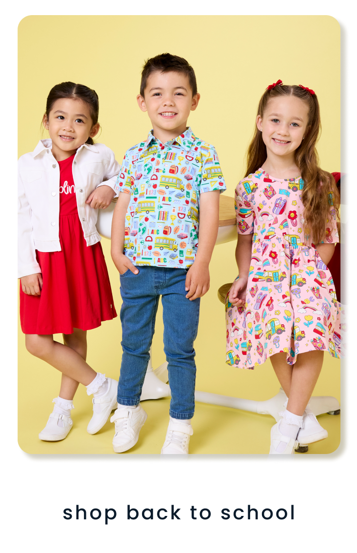 "Three children wearing back-to-school apparel, including a school-themed print polo, printed dress, and red dress with white jacket. Text below reads ‘shop back to school.’"