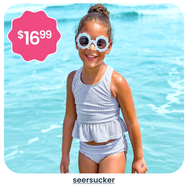 "Beach image showing a child in a blue and white striped seersucker two‑piece swimsuit in shallow water. A pink badge reads &lsquo;$16.99.&rsquo; Text below reads &lsquo;seersucker.&rsquo;"