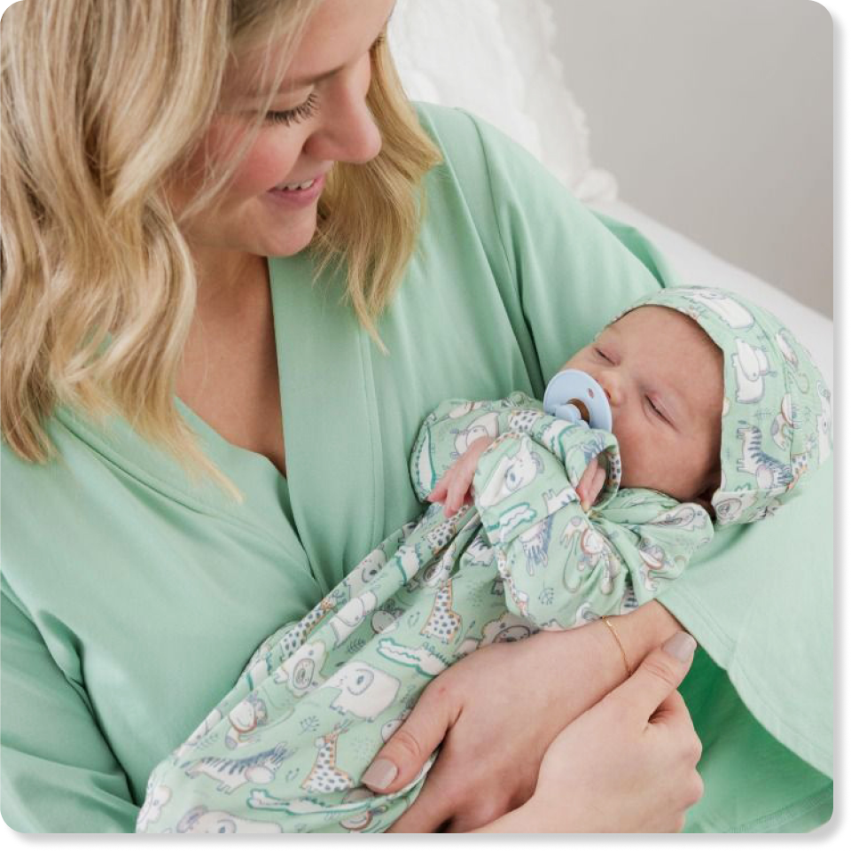 Promotional image showing an adult holding a newborn wearing a mint green animal‑print bamboo sleeper and hat. Featured as newborn essentials sleepwear and accessories